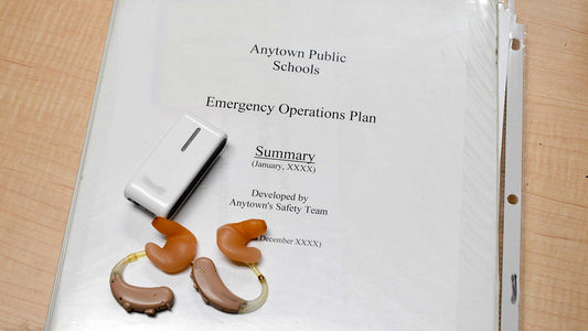 Three ring binder with coversheet Anytown Public Schools Emergency Operations Plan with 2 hearing aids and an external microphone.