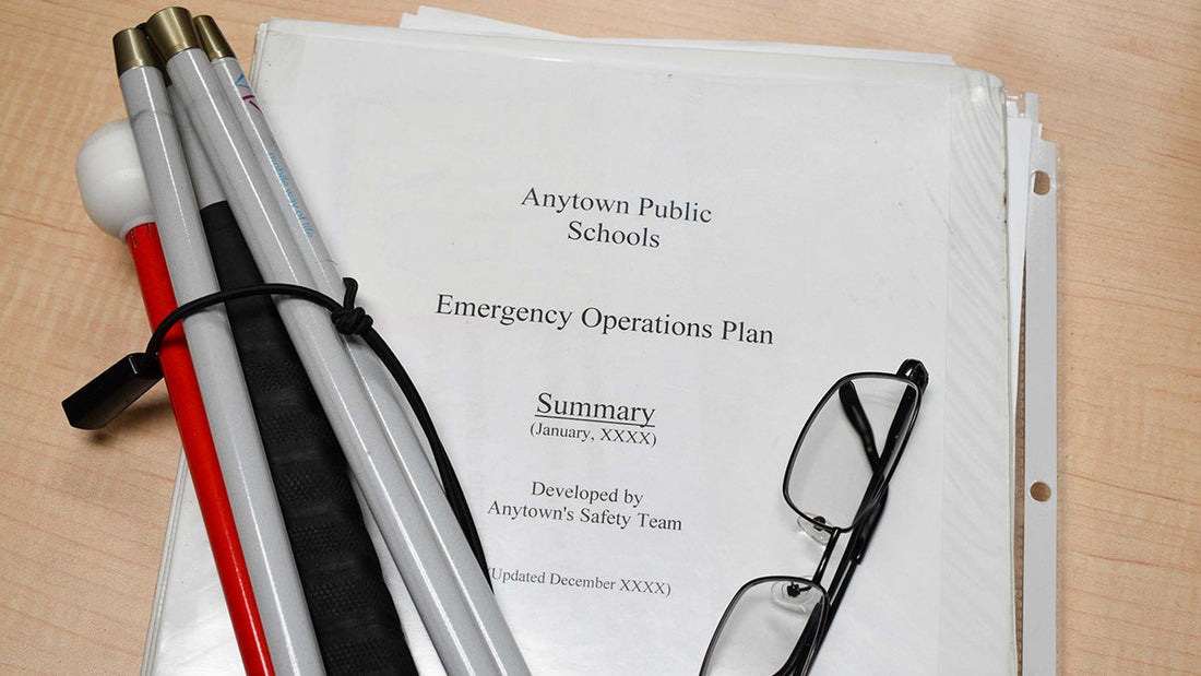 Three ring binder with coversheet Anytown Public Schools Emergency Operations Plan with folded white cane and folded wire rimmed glasses.