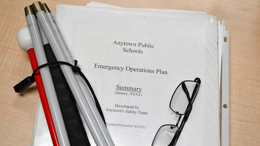 Three ring binder with coversheet Anytown Public Schools Emergency Operations Plan with folded white cane and folded wire rimmed glasses.
