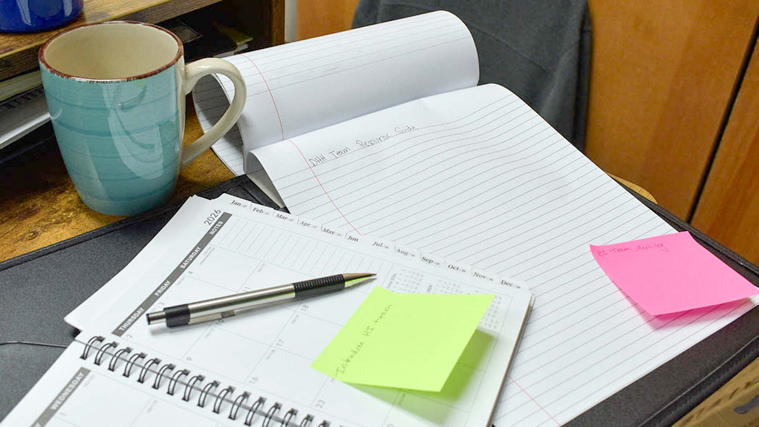 notebook with words DHH team resource guide written on it beside a pen and planner with sticky notes and coffee cup on desktop
