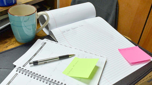 notebook with words DHH team resource guide written on it beside a pen and planner with sticky notes and coffee cup on desktop
